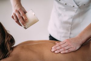 Physiotherapist drips wax from candle and massaging female patientâ€™s back.